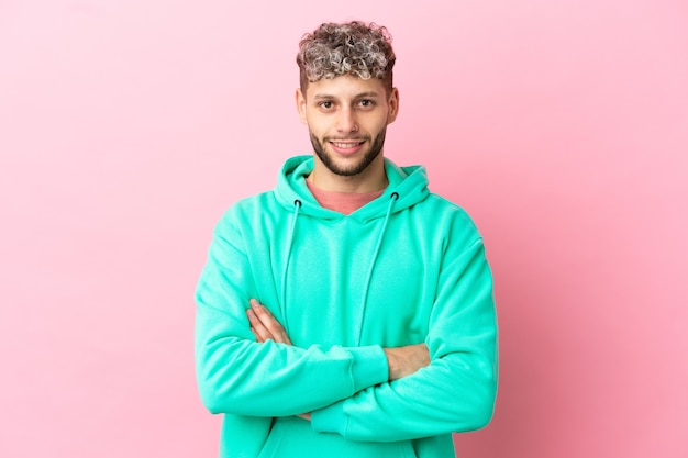 Jovem bonito homem caucasiano isolado em um fundo rosa, mantendo os braços cruzados na posição frontal