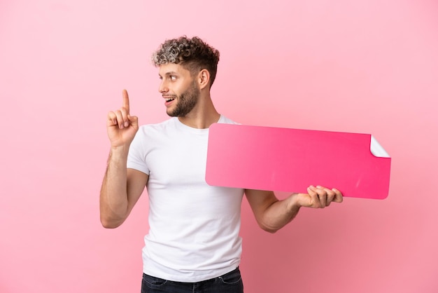 Jovem bonito homem caucasiano isolado em um fundo rosa segurando um cartaz vazio e pensando