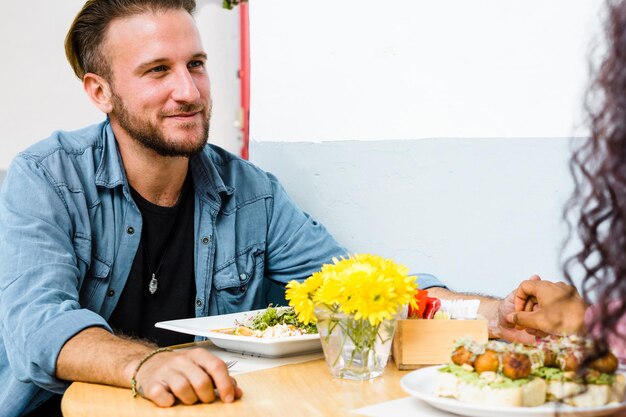 Jovem bonito homem caucasiano sorrindo e comendo em um restaurante.