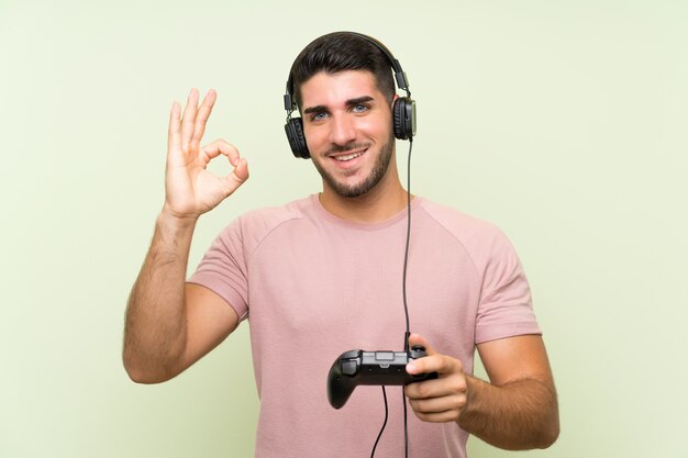 Jovem, bonito, homem, tocando, com, um, videogame controlador, ligado, parede verde, mostrando, tá bom sinal, com, dedos
