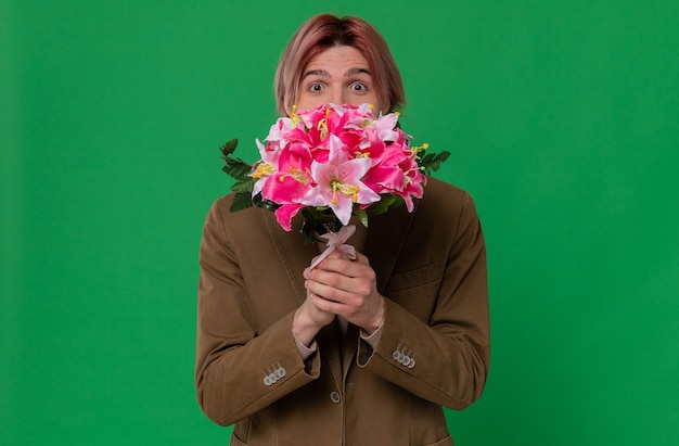 Jovem bonito impressionado segurando um buquê de flores e olhando