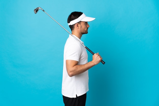 Jovem bonito isolado em uma parede azul jogando golfe em posição lateral