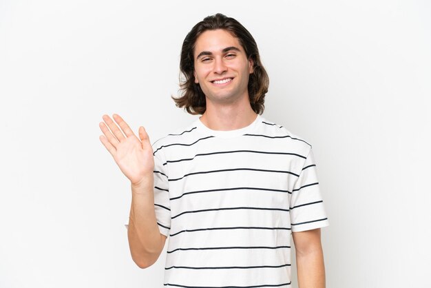 Jovem bonito isolado no fundo branco saudando com a mão com expressão feliz