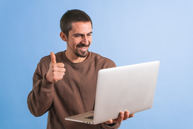 Jovem bonito isolado sobre um fundo azul usando seu laptop trabalhando Copie o texto do espaço