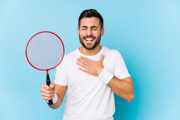 Jovem bonito jogando badminton ri alto, mantendo a mão no peito.