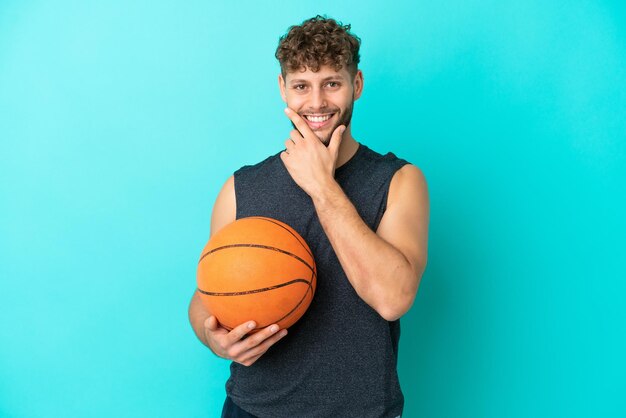 Jovem bonito jogando basquete isolado em fundo azul feliz e sorridente