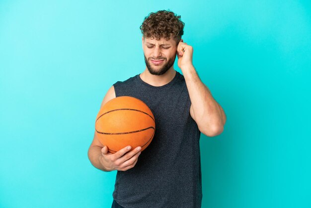 Jovem bonito jogando basquete isolado em fundo azul frustrado e cobrindo os ouvidos