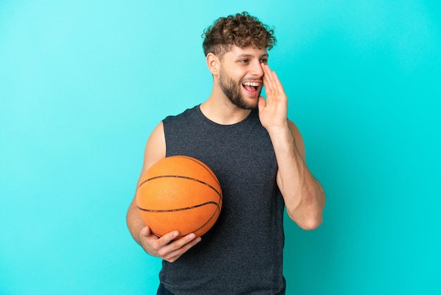 Jovem bonito jogando basquete isolado em um fundo azul, gritando com a boca bem aberta para o lado