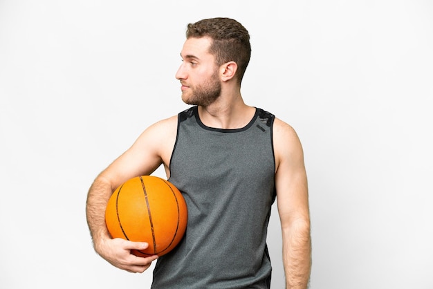 Jovem bonito jogando basquete sobre fundo branco isolado, olhando para o lado