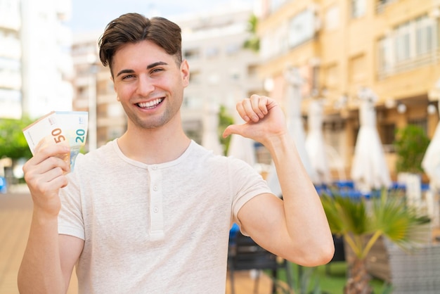 Jovem bonito levando muito dinheiro ao ar livre orgulhoso e satisfeito