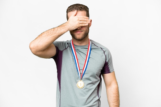 Jovem bonito loiro com medalhas sobre fundo branco isolado, cobrindo os olhos pelas mãos Não quero ver algo