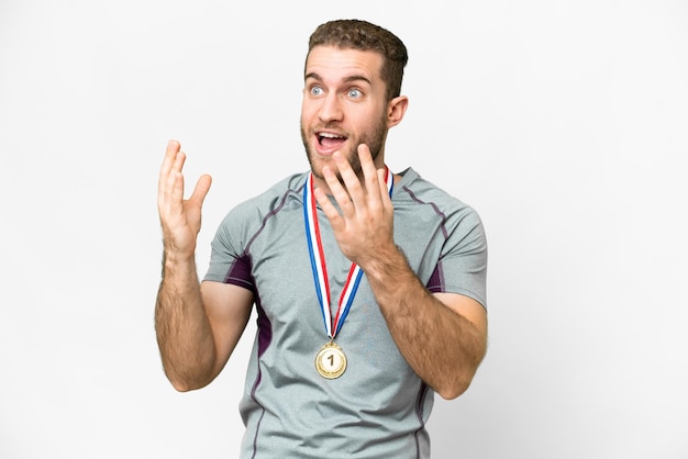 Jovem bonito loiro com medalhas sobre fundo branco isolado com expressão facial de surpresa