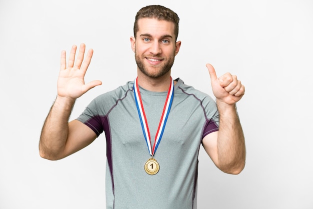 Jovem bonito loiro com medalhas sobre fundo branco isolado, contando seis com os dedos