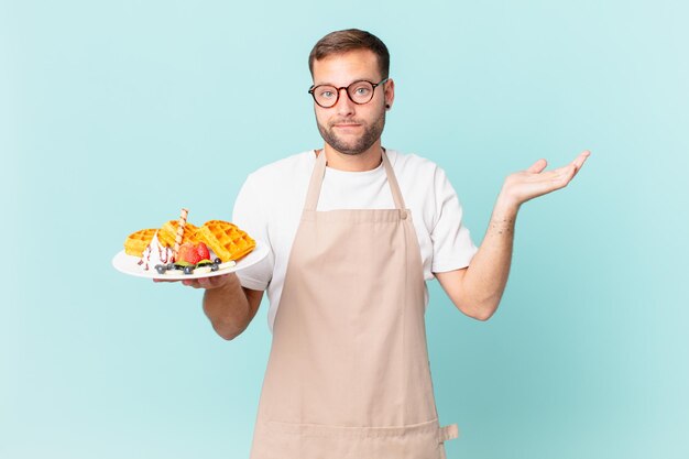 Jovem bonito loiro sentindo-se perplexo, confuso e duvidoso. cozinhar waffles conceito