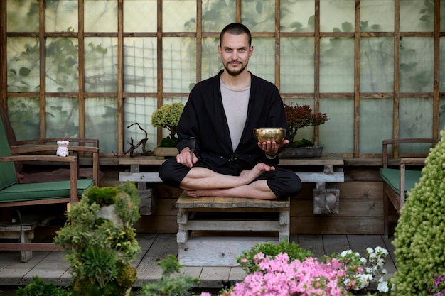 Jovem bonito meditando com uma tigela cantando em um gazebo gaden