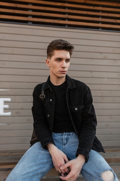 Jovem bonito na jaqueta jeans da moda em jeans elegantes azuis com mochila