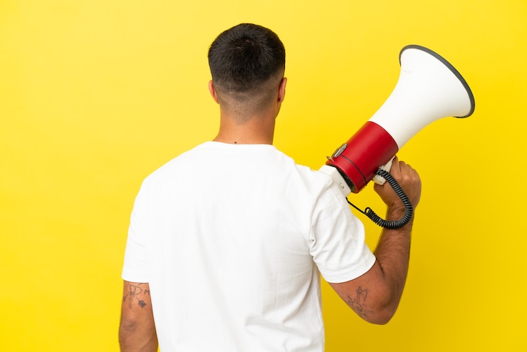 Foto jovem bonito na parede amarela isolada segurando um megafone e na posição traseira