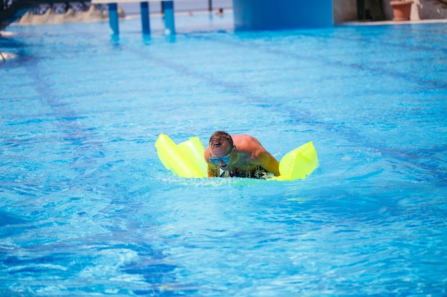Jovem bonito nadando em colchão inflável na piscina azul