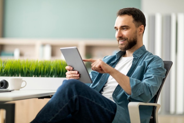 Jovem bonito navegando na internet em tablet digital no escritório