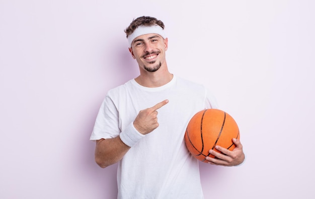 Jovem bonito olhando animado e surpreso apontando para o lado. conceito de basquete