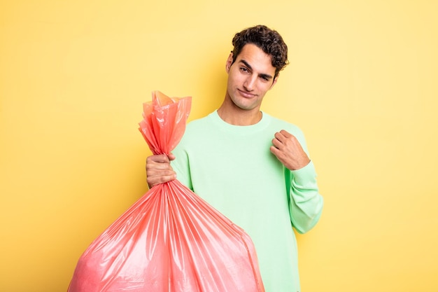 Jovem bonito olhando arrogante conceito de saco de lixo positivo e orgulhoso bem sucedido