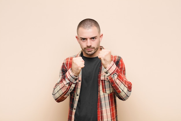 Jovem bonito olhando confiante, irritado, forte e agressivo, com os punhos prontos para lutar em posição de boxe contra a parede