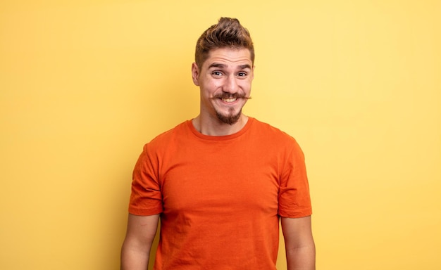 jovem bonito olhando feliz e pateta com um sorriso largo, divertido e maluco e olhos bem abertos. conceito de bigode estranho