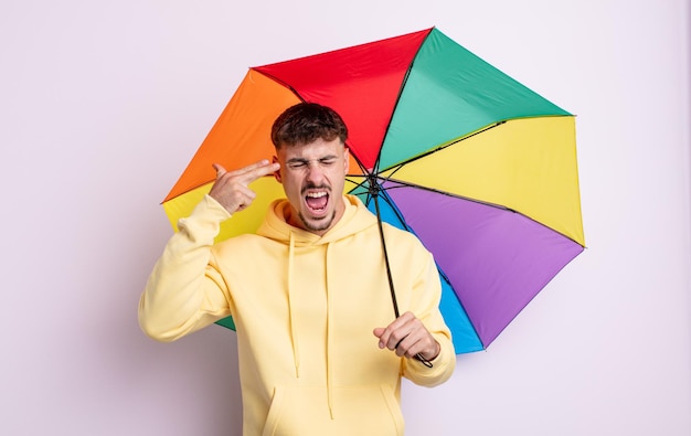 Jovem bonito olhando infeliz e estressado, gesto de suicídio fazendo sinal de arma. conceito de guarda-chuva