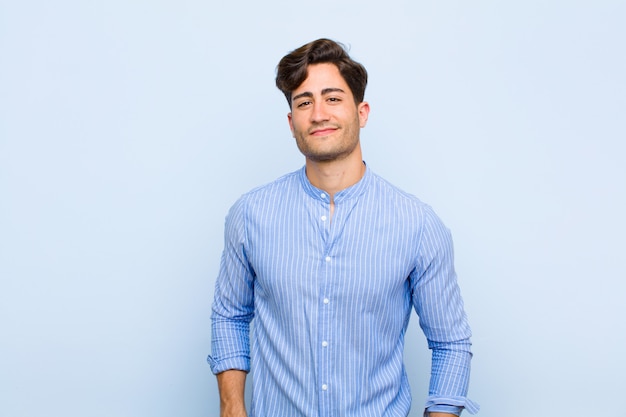 Jovem bonito olhando orgulhoso, confiante, legal, atrevido e arrogante, sorrindo, sentindo-se bem sucedido sobre parede azul