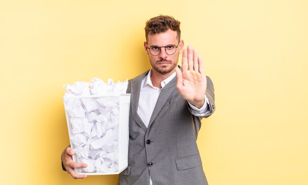 Jovem bonito olhando sério mostrando a palma aberta fazendo gesto de parada bolas de papel conceito de lixo