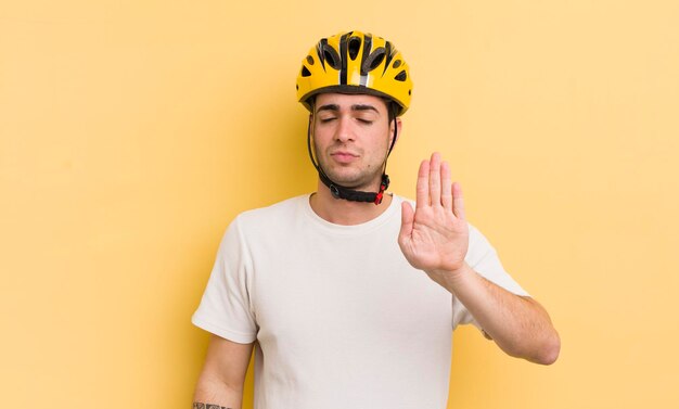 Jovem bonito olhando sério mostrando a palma da mão aberta fazendo o conceito de bicicleta de gesto de parada