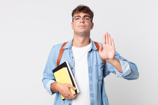 Jovem bonito olhando sério mostrando a palma da mão aberta, fazendo o gesto de parada. conceito de estudante universitário