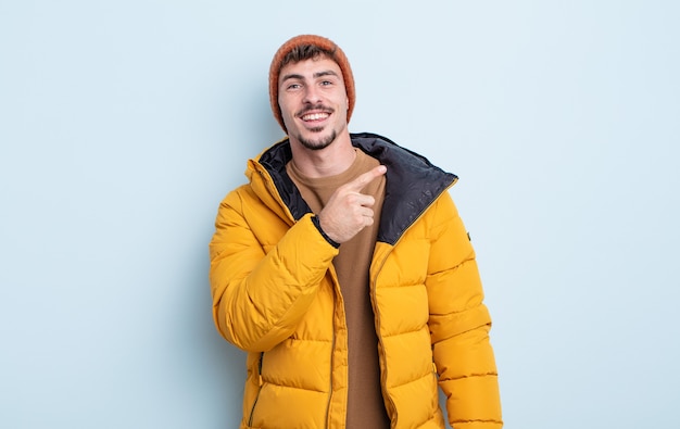 Jovem bonito parecendo animado e surpreso, apontando para o lado. conceito de inverno