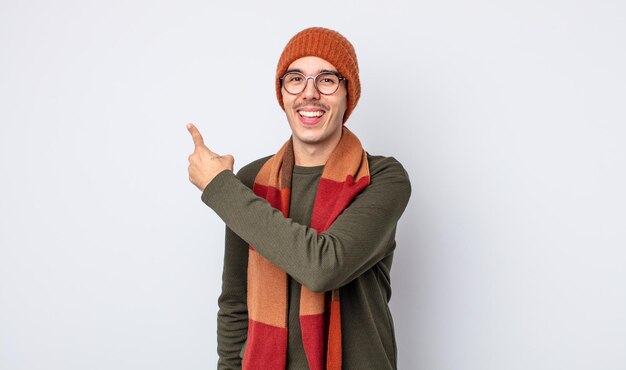 Jovem bonito parecendo animado e surpreso, apontando para o lado. conceito de roupas de inverno