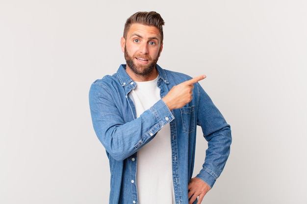 Jovem bonito parecendo animado e surpreso apontando para o lado