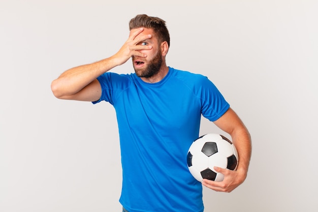 Jovem bonito parecendo chocado, assustado ou apavorado, cobrindo o rosto com a mão. conceito de futebol