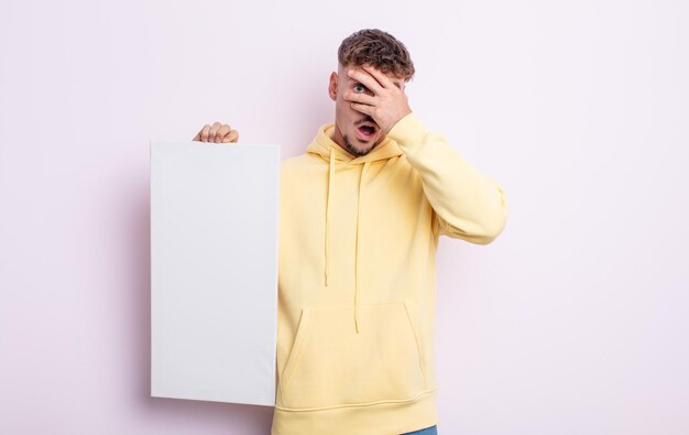 Jovem bonito parecendo chocado, assustado ou apavorado, cobrindo o rosto com a mão. conceito de tela em branco