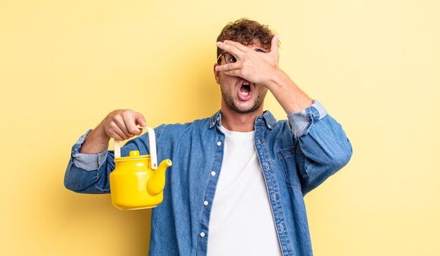 Jovem bonito parecendo chocado, assustado ou apavorado, cobrindo o rosto com a mão.