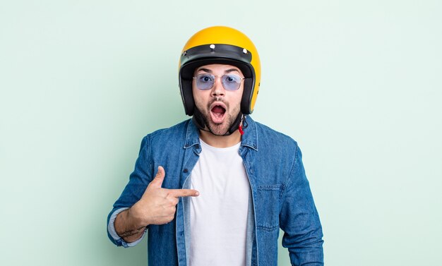 Jovem bonito parecendo chocado e surpreso com a boca aberta, apontando para si mesmo. conceito de capacete de motocicleta