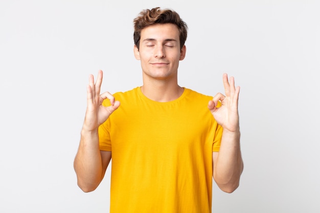 Jovem bonito parecendo concentrado e meditando, sentindo-se satisfeito e relaxado, pensando ou fazendo uma escolha