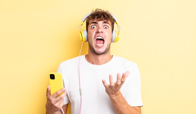 Jovem bonito parecendo desesperado, frustrado e estressado. conceito de fones de ouvido e smartphone