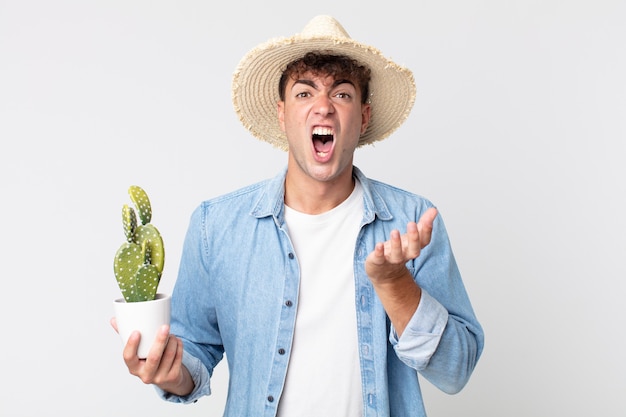 Jovem bonito parecendo desesperado, frustrado e estressado. fazendeiro segurando um cacto decorativo