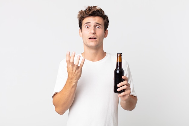 Foto jovem bonito parecendo desesperado, frustrado e estressado segurando uma garrafa de cerveja