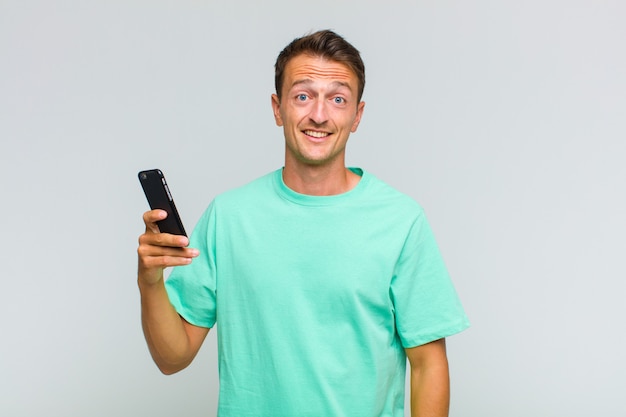 Jovem bonito parecendo feliz e agradavelmente surpreso, animado com uma expressão de fascínio e choque