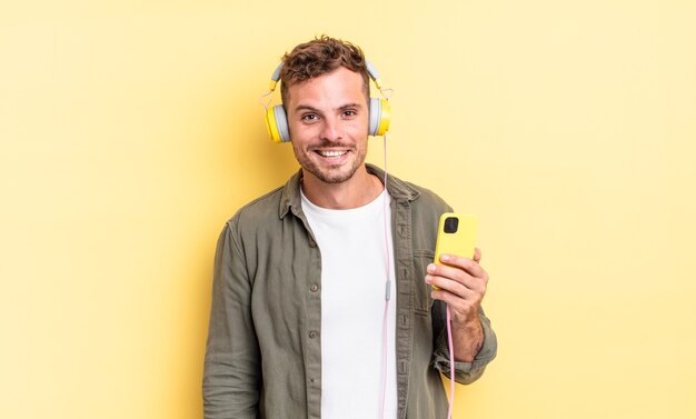 Jovem bonito parecendo feliz e agradavelmente surpreso com fones de ouvido e conceito de smartphone