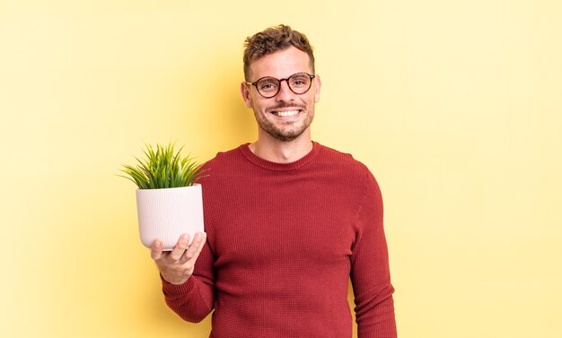 Jovem bonito parecendo feliz e agradavelmente surpreso. conceito de planta decorativa