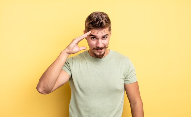 Jovem bonito parecendo feliz, espantado e surpreso, sorrindo e percebendo uma boa notícia incrível. conceito de bigode estranho