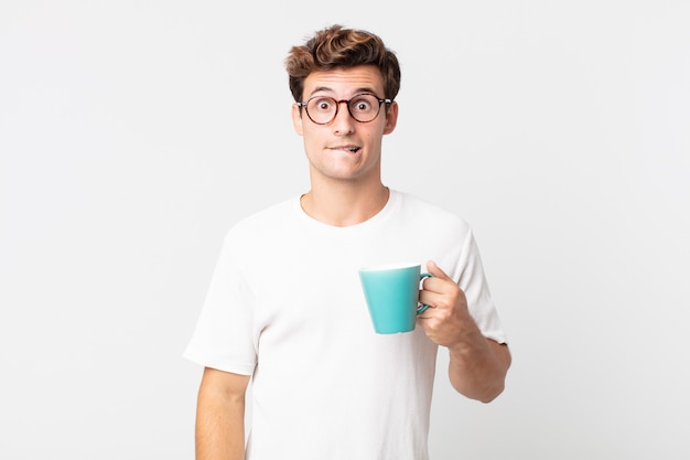 Jovem bonito parecendo perplexo e confuso e segurando uma xícara de café