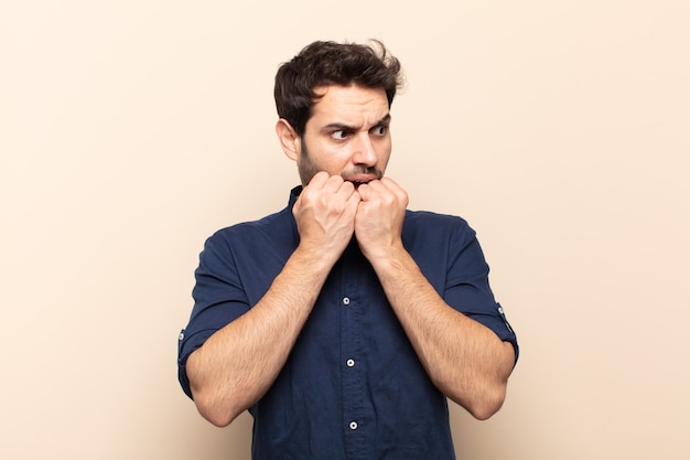 Jovem bonito parecendo preocupado, ansioso, estressado e com medo, roendo as unhas e olhando para o espaço da cópia lateral