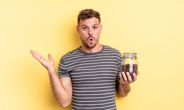 Jovem bonito parecendo surpreso e chocado, com o queixo caído segurando um objeto conceito de grãos de café